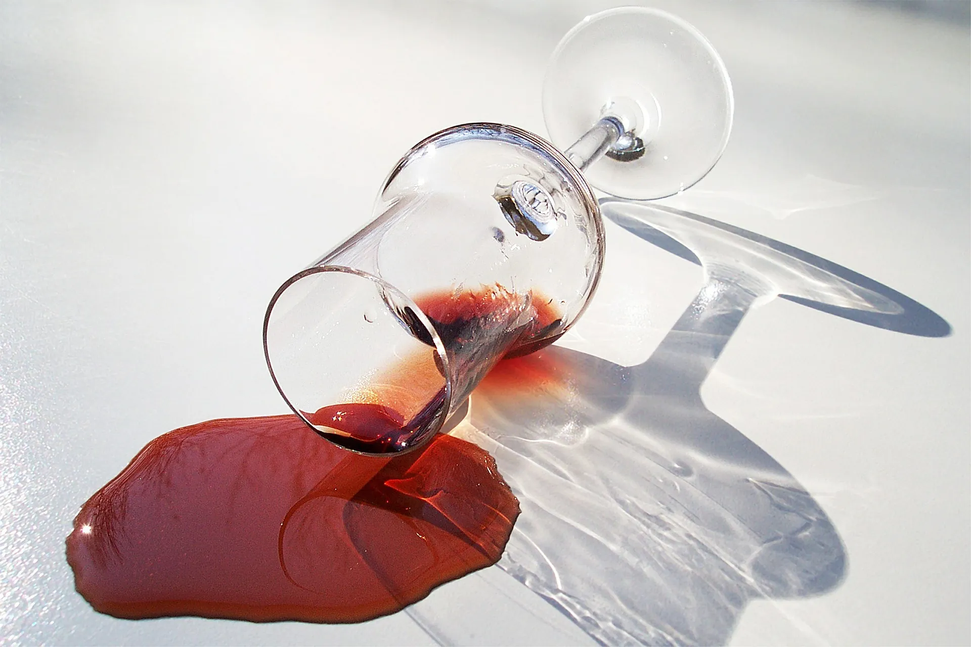 Close-up of a tipped wine glass with red liquid spilling onto a white surface, red and white tones, dramatic still-life
