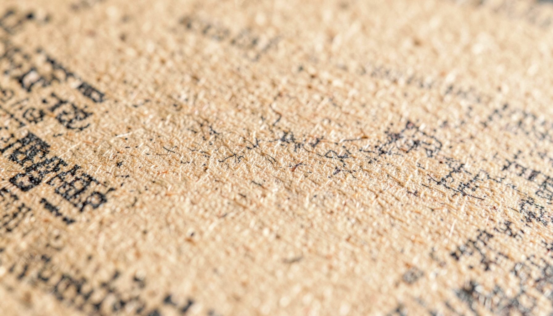 Close-up texture of aged newsprint paper with visible fiber grain, in warm sandy tan and charcoal tones, quiet and archi