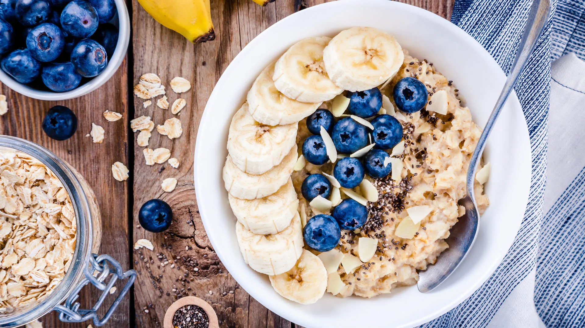 Overhead view of a bowl of oatmeal topped with banana slices, blueberries and nuts on a wooden table